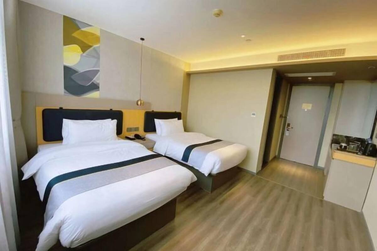 A hotel room with two beds, a small kitchenette, and a door leading to another room.