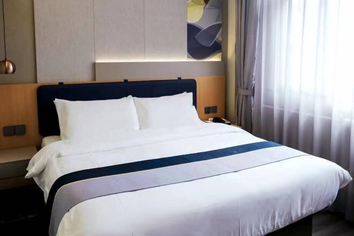 A hotel room with a bed, a nightstand, a lamp, and a window with curtains.