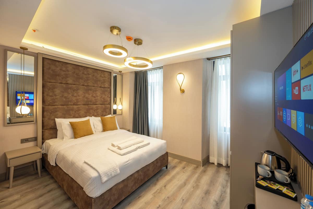 Una habitación de hotel moderna con una cama grande, mesitas de noche, un televisor de pantalla plana y un aplique de techo.