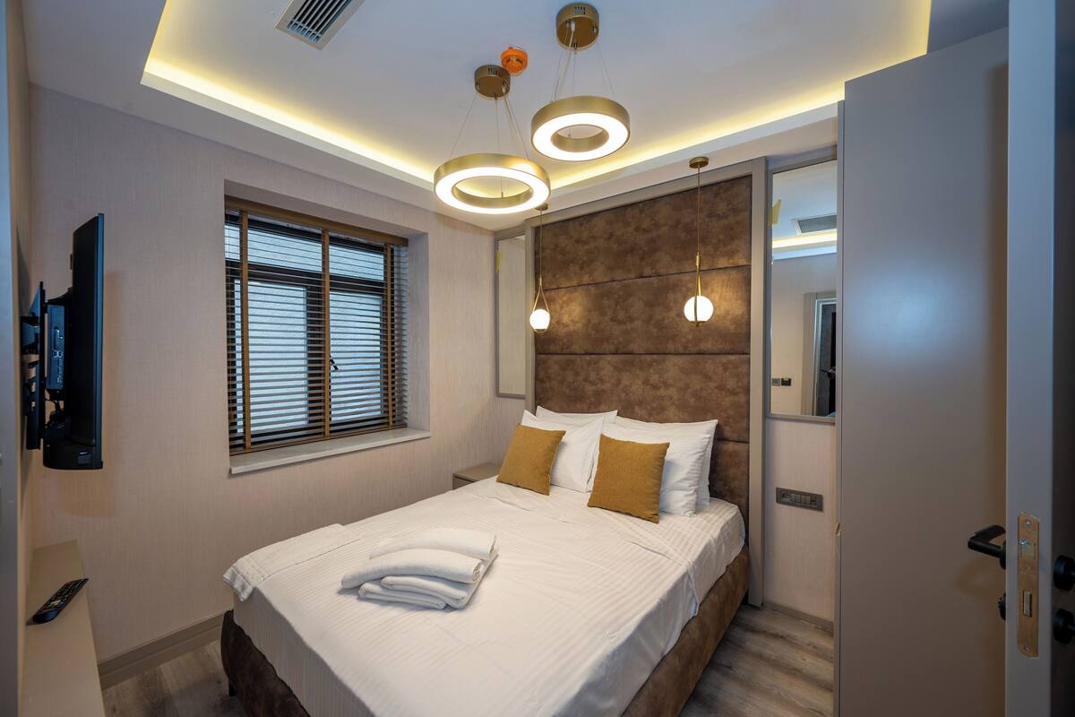 Un dormitorio moderno con una cama grande, un televisor en la pared y una ventana con persianas.
