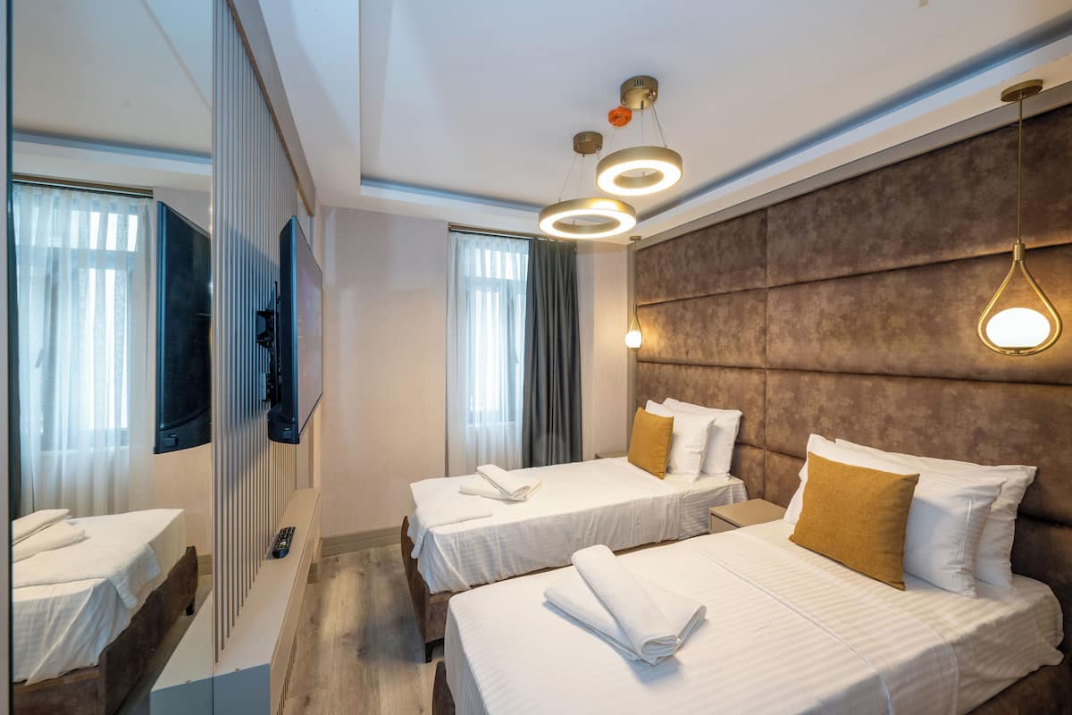 Habitación de hotel con dos camas, un espejo grande, un televisor de pantalla plana y una lámpara moderna.