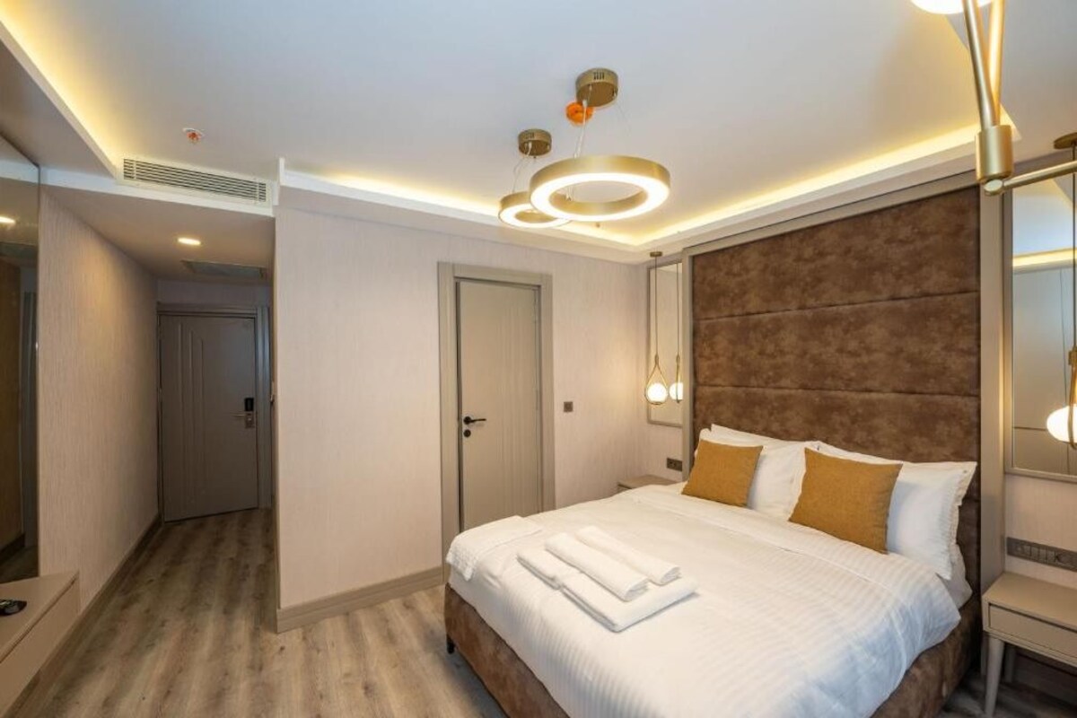 Een moderne hotelkamer met een groot bed, een houten hoofdbord en een plafondlamp.