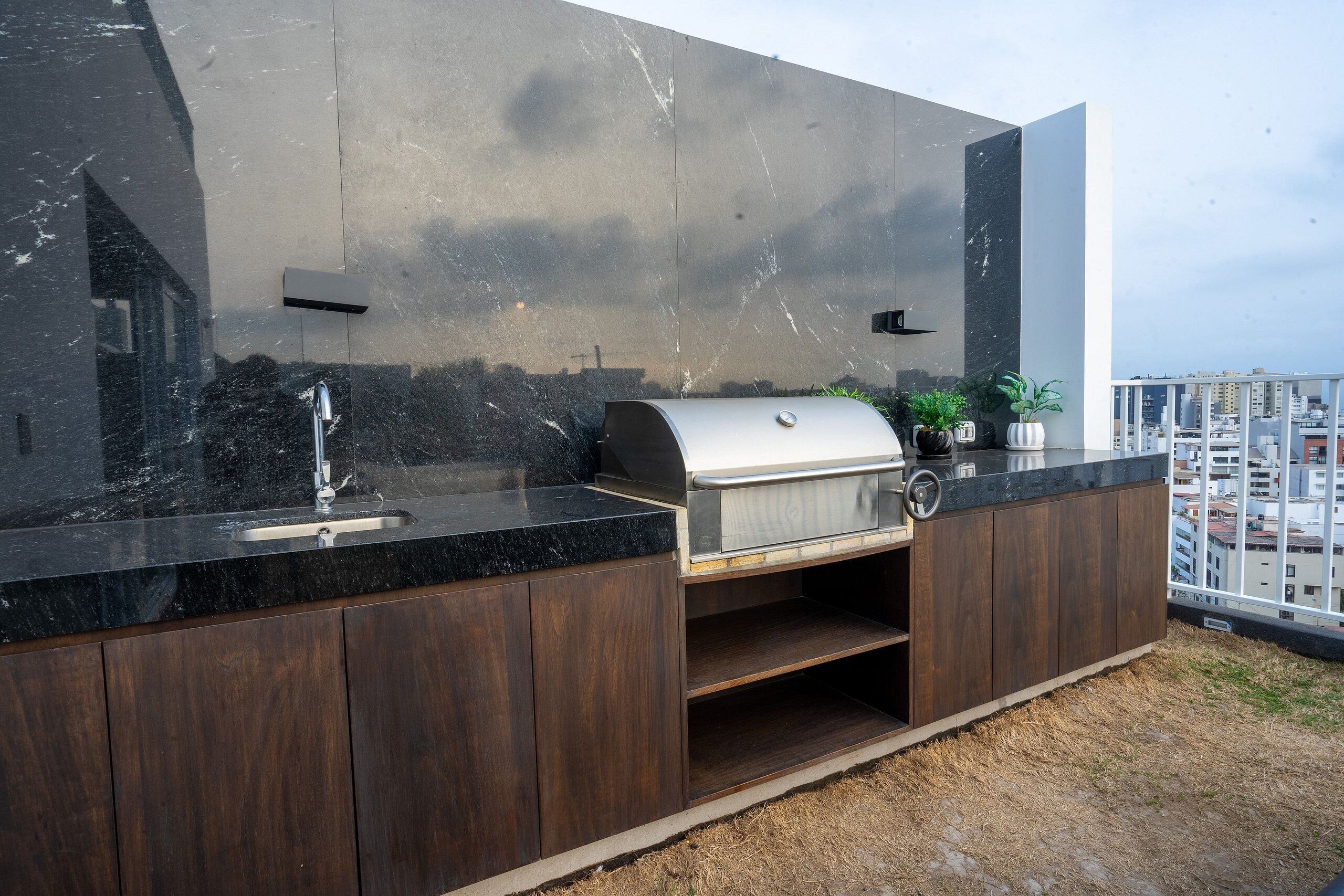 Una cocina exterior moderna con pileta, parrilla y muebles bajos de madera.