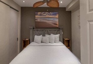 Ein Schlafzimmer mit Bett, Kopfteil, zwei Nachttischen und Deckenventilator.