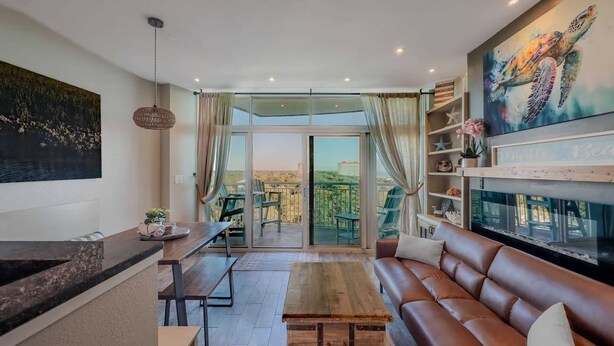 Una sala de estar moderna con una mesa de centro de madera, un sofá de cuero marrón, una zona de comedor con un banco y un ventanal con vistas al exterior.