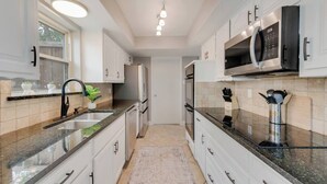 A modern kitchen with white cabinets, granite countertops, a stainless steel refrigerator, and a microwave.
