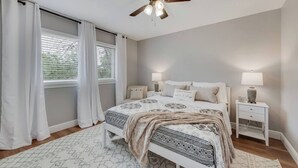 A bedroom with a bed, two bedside tables, a ceiling fan, and a window with curtains.