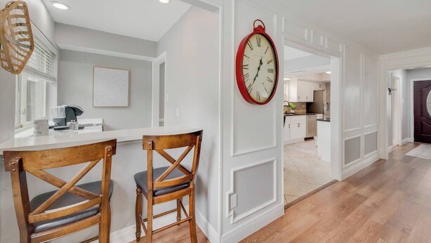 A kitchen with white cabinetry, a red clock, and two wooden chairs.