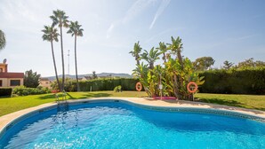 A swimming pool with a clear blue water, surrounded by a well-maintained lawn, palm trees, and a hedge. - Gunilla townhouse no 6 (Manilva)