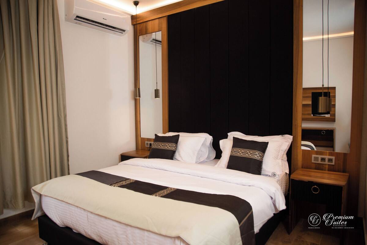 A hotel room with a large bed, a wooden headboard, a mirror, a nightstand, and an air conditioning unit.