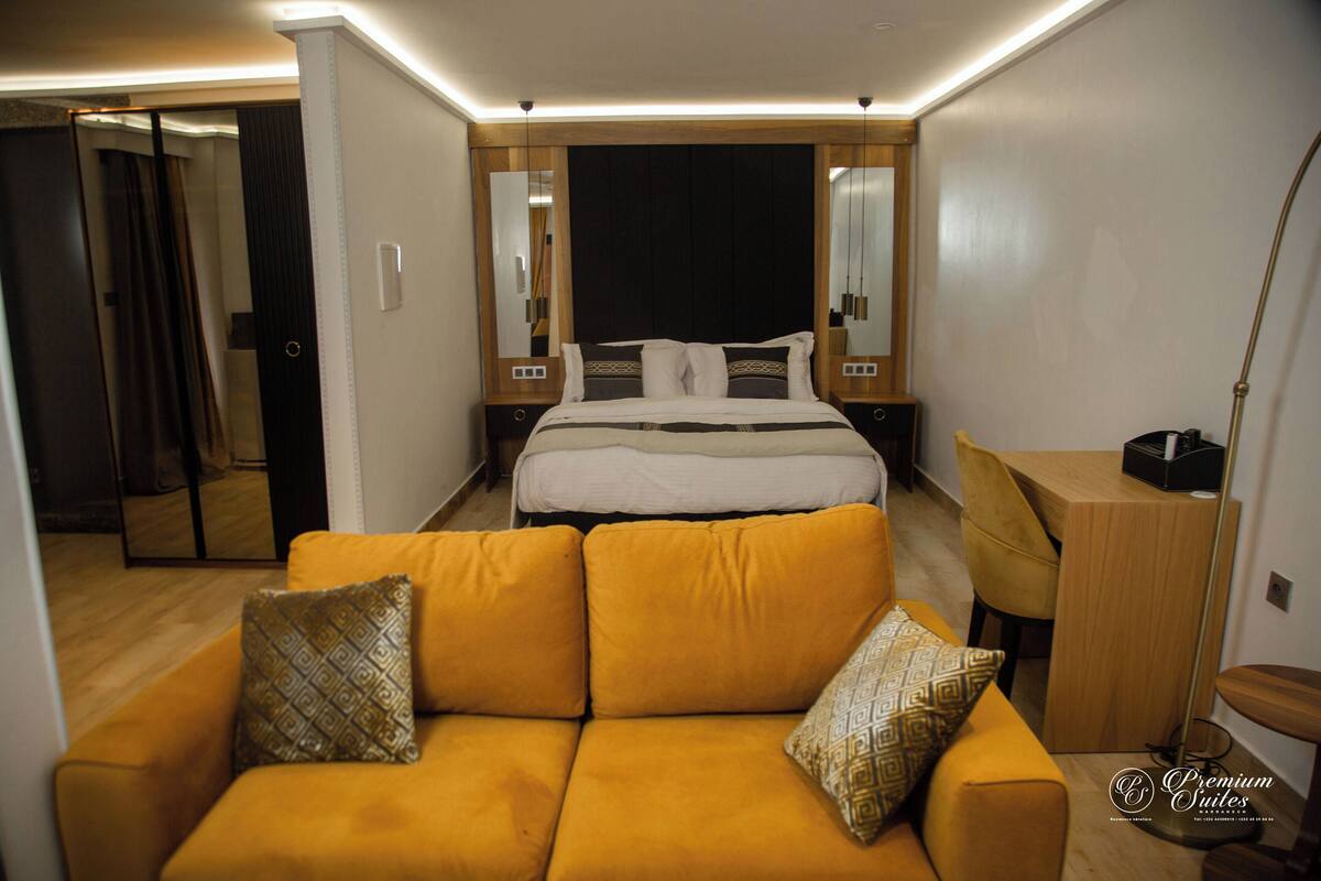 A modern hotel room with a large bed, a sofa, a desk, and a mirror.
