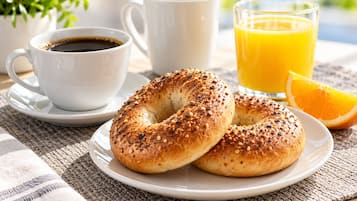 A breakfast setting with a plate of bagels, a cup of coffee, a glass of orange juice, and a slice of orange.