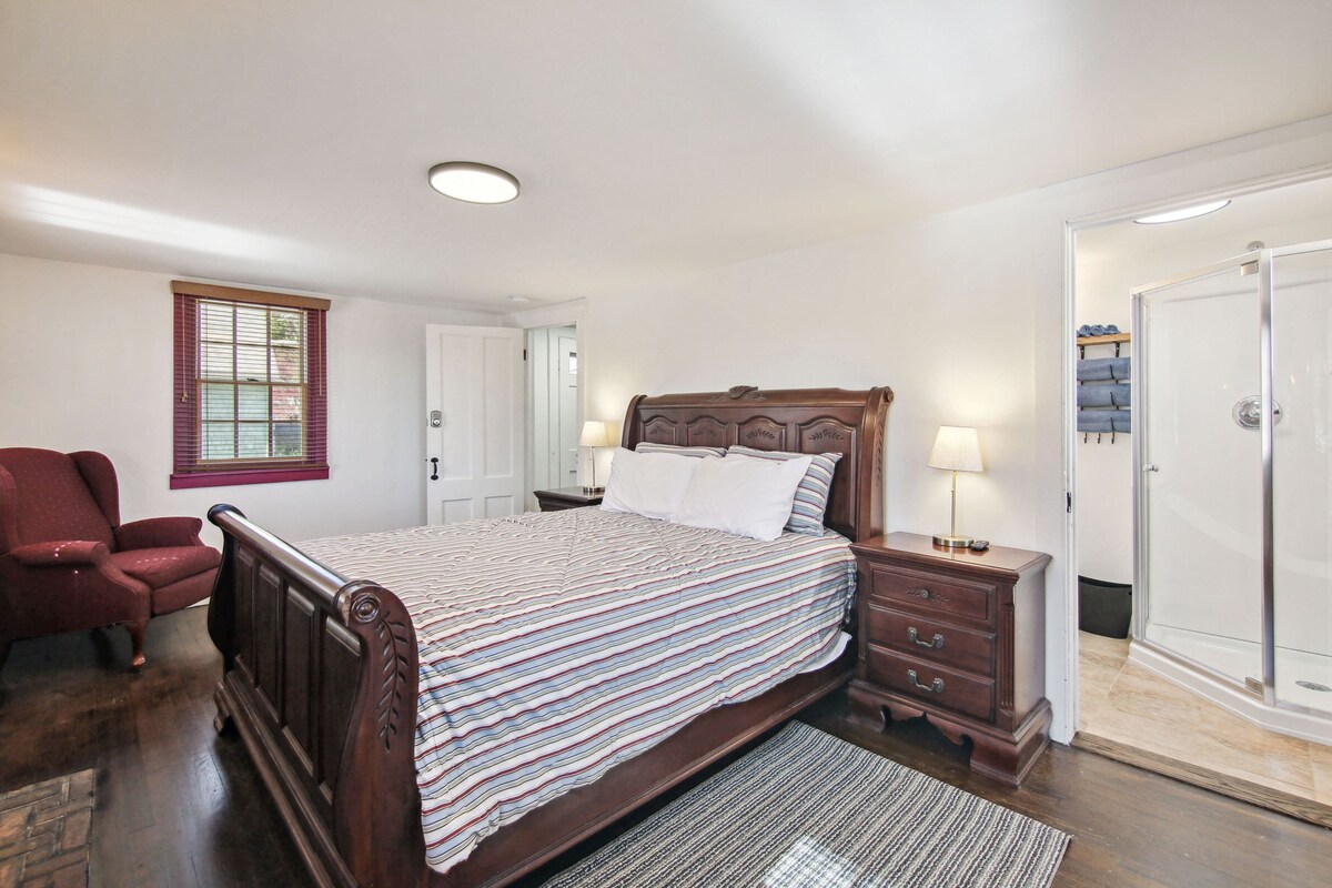 A bedroom with a wooden bed, a nightstand, a chair, and a door leading to a bathroom.