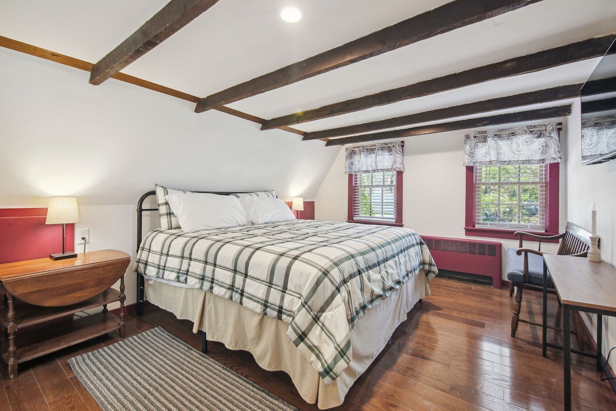 A bedroom with a bed, wooden furniture, a window with lace curtains, and a red wall.