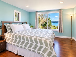A bedroom with a large bed, a nightstand, a bedside lamp, a window with curtains, and a view of the outdoors. - The Cottage Inn At Amos Lake (Preston)