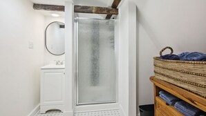 A bathroom with a glass shower enclosure, a white vanity, a wooden shelf with towels, and a ceiling skylight. - The Cottage Inn At Amos Lake (Preston)