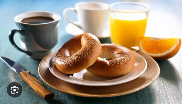 A breakfast setting with a plate of bagels, a cup of coffee, a glass of orange juice, and a half orange on a wooden table. - The Cottage Inn At Amos Lake (Preston)
