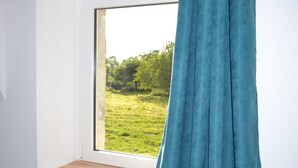 A window with a view of a grassy field and trees. - Gîte 6 Personnes Chaleureux et au Calme à 15 Minutes des Plages du Débarquement (Picauville)