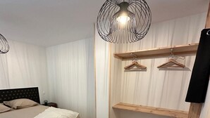 A bedroom with a bed, a bench, a hanging light fixture, wooden shelves, and a basket. - Gîte 6 Personnes Chaleureux et au Calme à 15 Minutes des Plages du Débarquement (Picauville)