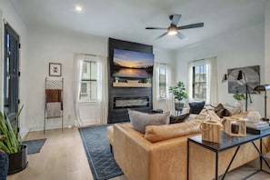 Una sala de estar moderna con sofá, chimenea, ventilador de techo y vistas al exterior.