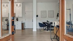 A spacious kitchen with white cabinets, a dining area with a table and chairs, and a hallway leading to a door.