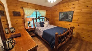 Ein gemütliches Schlafzimmer im Chalet-Stil mit einem Holzbettengestell, einem Nachttisch mit Lampe, einem Fenster mit Vorhängen und einem Deckenventilator.
