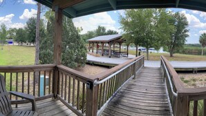 A wooden deck with a view of a park area, including picnic tables and a covered pavilion. - Jiggs Landing, Cabin 4 - Old World Waterside Double (Manatee County)