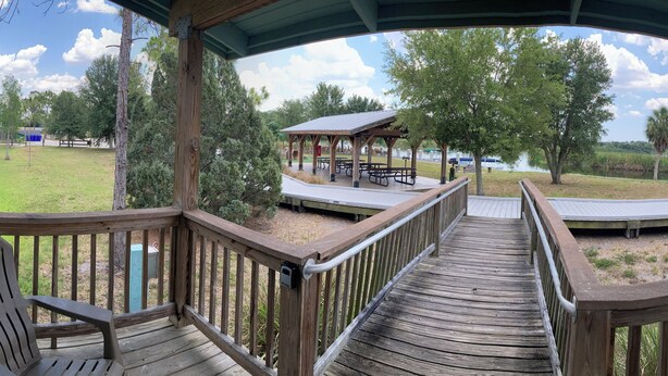 En træterrasse med udsigt over en park, der inkluderer picnicborde og en overdækket pavillon.