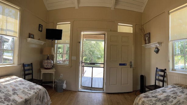 Una habitación con dos camas, televisión, puerta que da al exterior y ventana con vista a árboles.