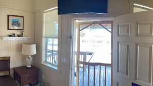 A room with a wooden door, a window, a lamp, a chair, and a shelf with decorative items. - Jiggs Landing, Cabin 3 - Reservoir View Bunk House (Manatee County)