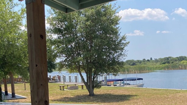 A wooden deck with a view of a lake, picnic tables, and a boat dock. - Jiggs Landing, Cabin 3 - Reservoir View Bunk House (Manatee County)