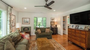 A living room with a sofa, armchair, ottoman, wooden dresser, television, and a ceiling fan.