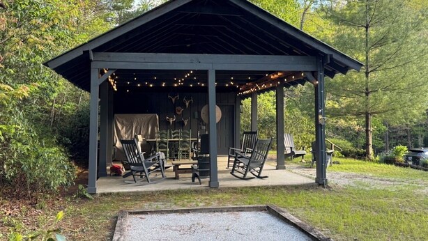A covered outdoor seating area with chairs and a table, surrounded by trees.