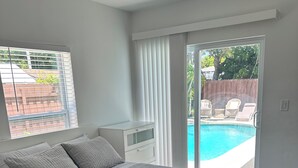 A bedroom with a bed, a nightstand, a window with blinds, and a view of a swimming pool. - Pool entire house 3bed 2bath and sofa bed  (North Miami Beach)