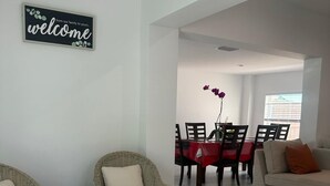 A living room with wicker chairs, a sofa, a dining table with chairs, and a 'welcome' sign. - Pool entire house 3bed 2bath and sofa bed  (North Miami Beach)
