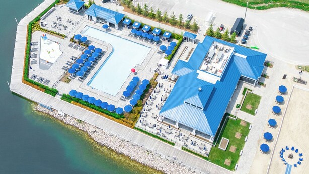An aerial view of a waterfront hotel with a pool, outdoor seating, and a parking area.