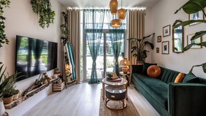 A living room with a green sofa, a TV, and various plants.