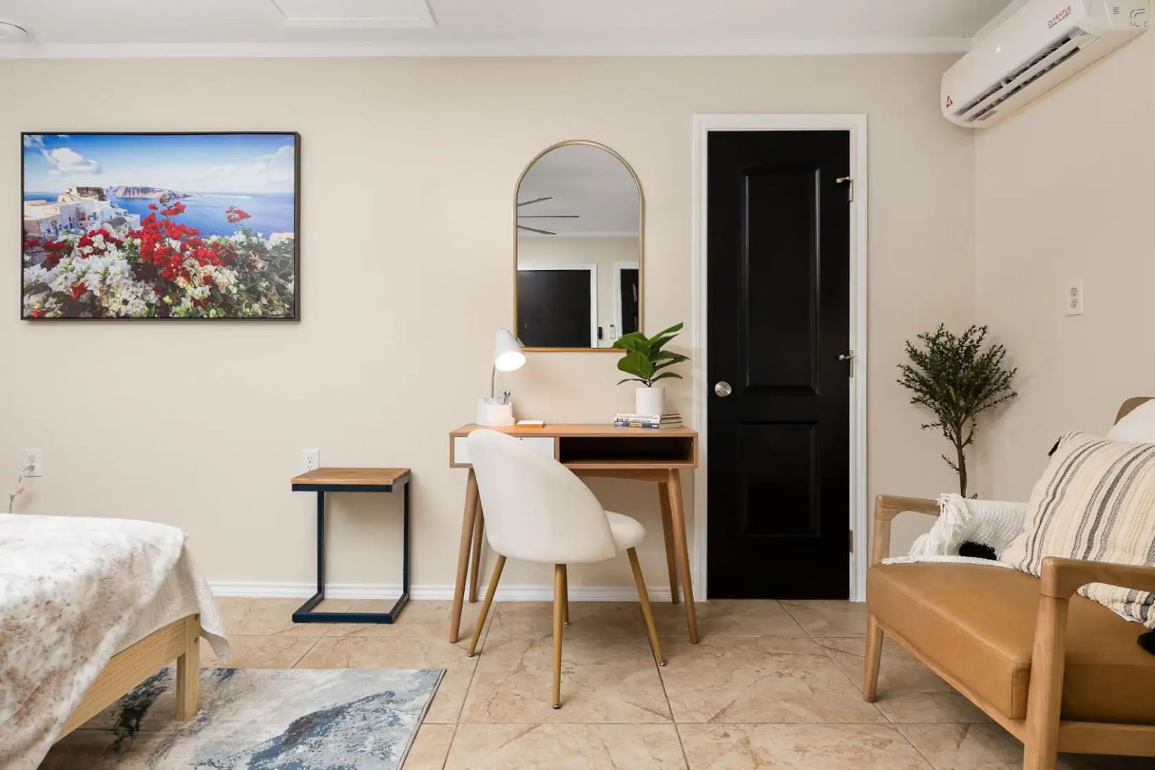 A modern bedroom with a bed, a desk with a chair, a mirror, and a door.