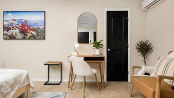 A modern bedroom with a bed, a desk with a chair, a mirror, and a door.