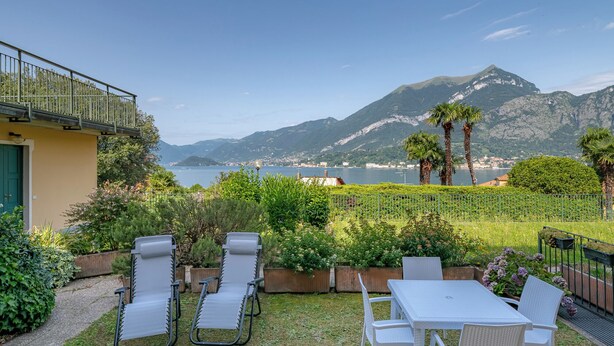 A patio with outdoor furniture, a view of the sea, and mountains in the background. - Swan Lake by Wonderful Italy (Bellagio)