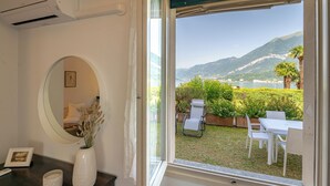 A room with a large window, a mirror, a vase with dried plants, and a small table with a picture frame. - Swan Lake by Wonderful Italy (Bellagio)