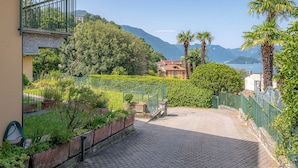 A cobblestone pathway leading to a building with a balcony, surrounded by lush greenery and a view of mountains and water. - Swan Lake by Wonderful Italy (Bellagio)