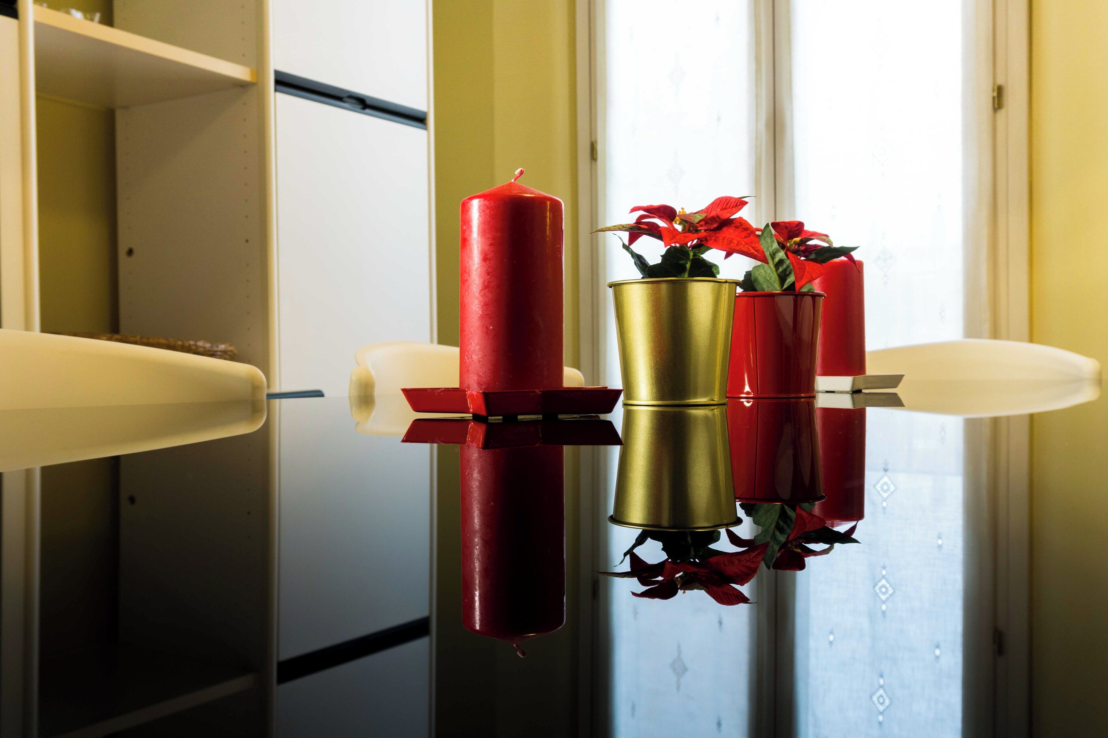 A room with a reflective surface, a red candle, and a flower arrangement in a gold pot.