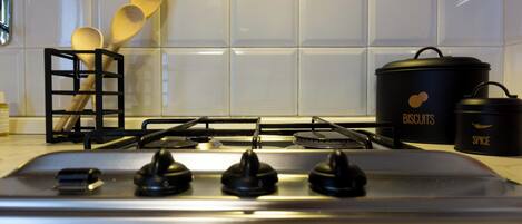 Una cocina con estufa a gas, un recipiente negro para especias y un contenedor negro con la etiqueta 'BISCUITS'.