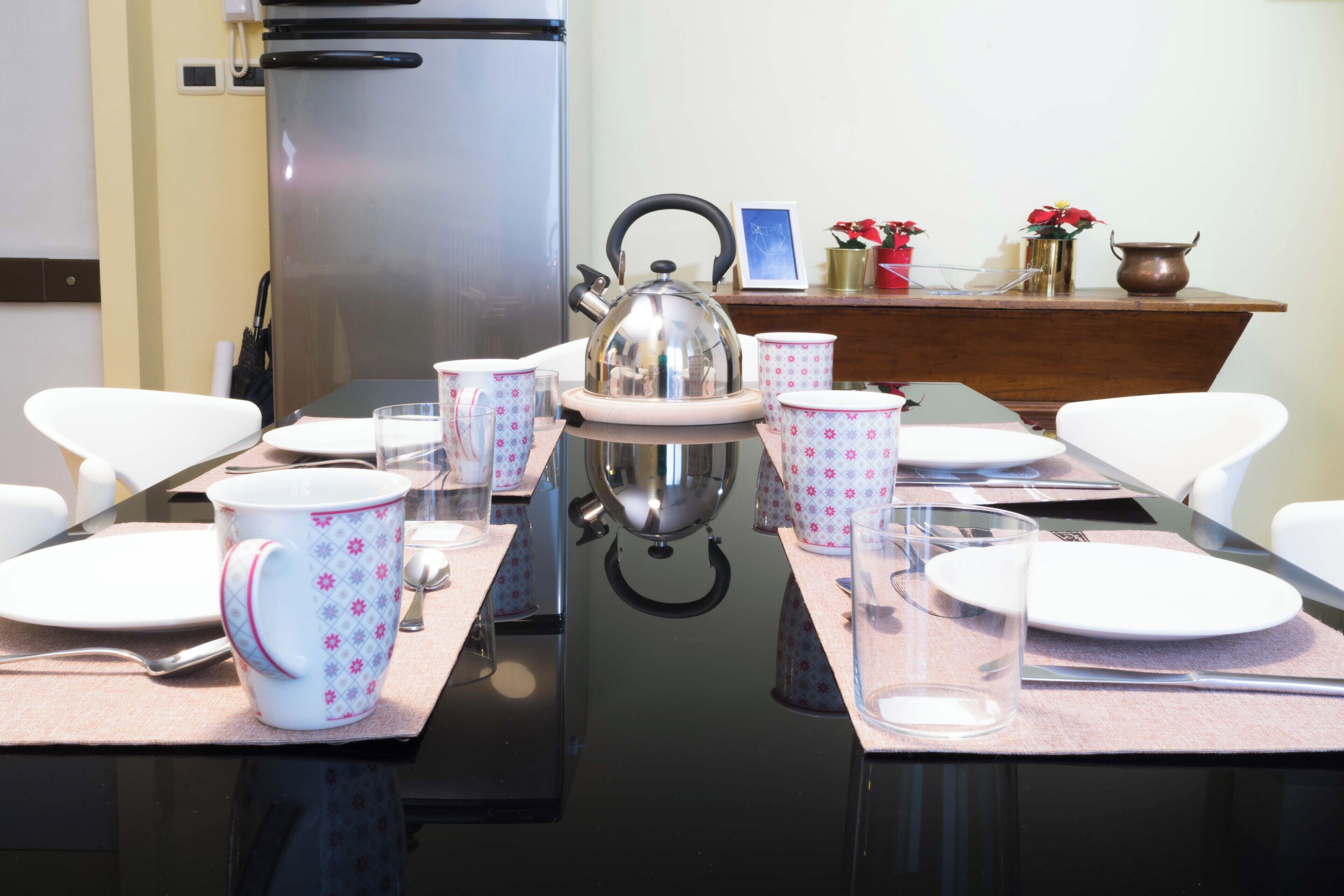 Una mesa de comedor dispuesta con platos blancos, tazas florales rosas y una tetera.