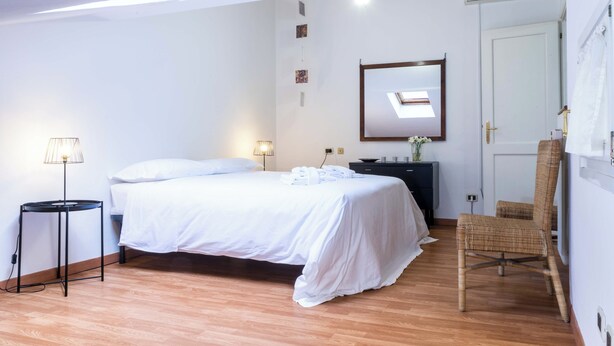 Een slaapkamer met een bed, nachtkastje, lamp, stoel, kapstok en een spiegel, plus een deur.