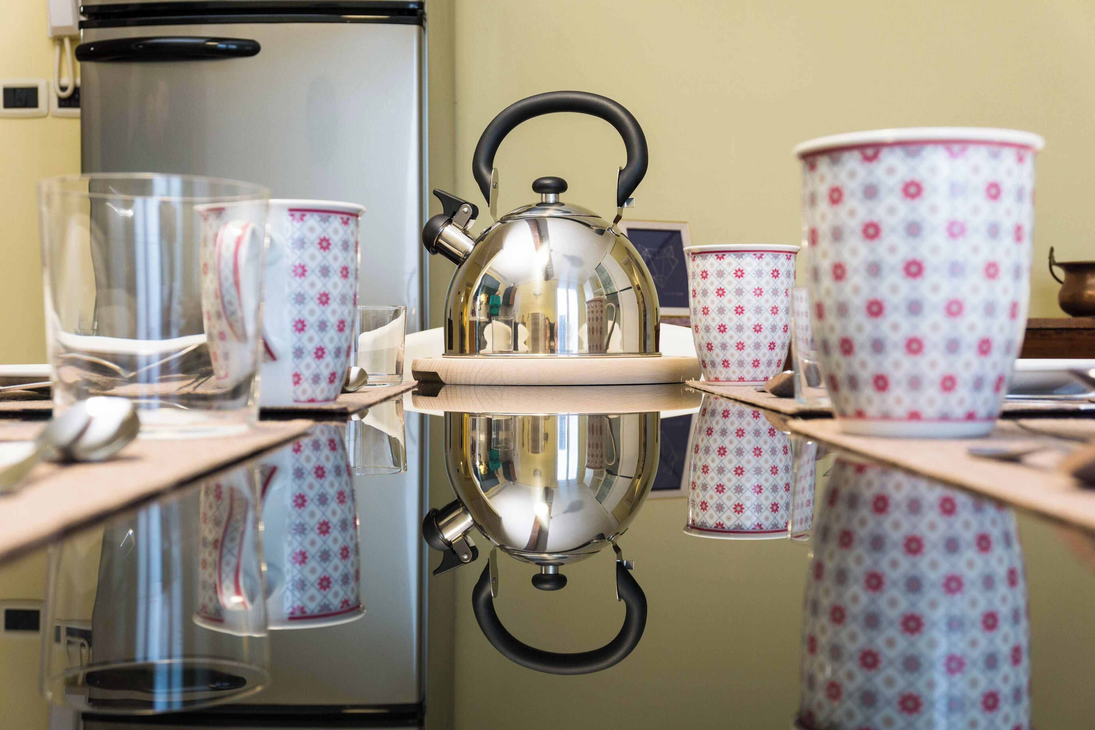 A kitchen counter with a kettle, cups, and a glass.