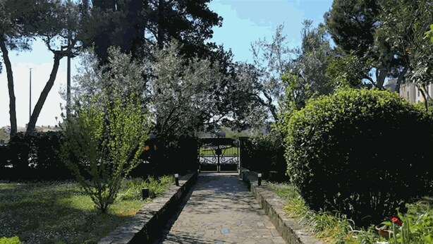A stone pathway leading to a gated entrance surrounded by trees and greenery.