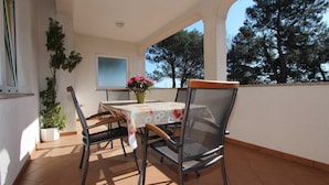 An outdoor patio with a table and chairs, a potted plant, and a view of trees.