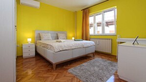 A bedroom with a bed, bedside tables, a radiator, a window with curtains, and a desk.